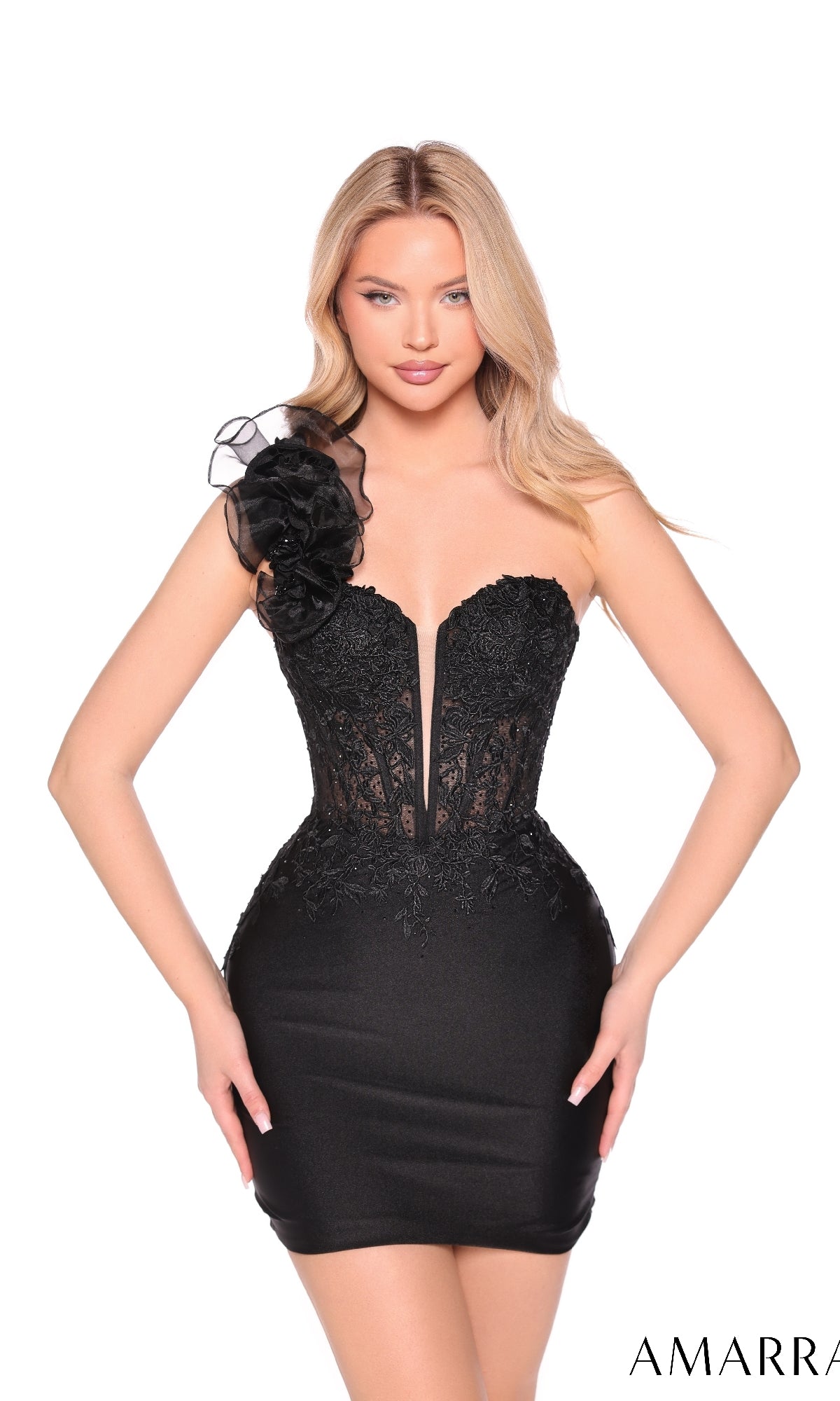 A woman models the Amarra 89005 One-Shoulder Mini Jersey Hoco Dress—black, form-fitting, with a sheer-lace bodice, deep V neckline, and large floral shoulder embellishment—against a white background.